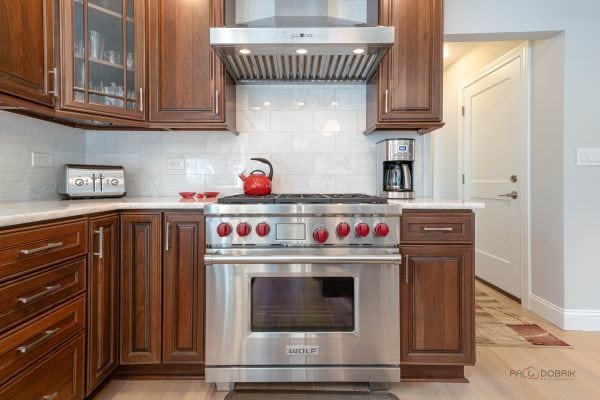 kitchen with premium stove, wall chimney exhaust hood, tasteful backsplash, and light countertops