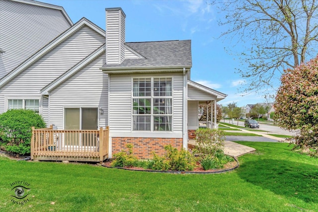 rear view of property featuring a deck, brick siding, a yard, a chimney, and a shingled roof