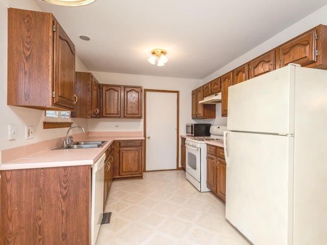 kitchen featuring brown cabinetry, a sink, light floors, under cabinet range hood, and white appliances