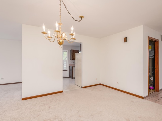 empty room featuring a notable chandelier, light colored carpet, and baseboards
