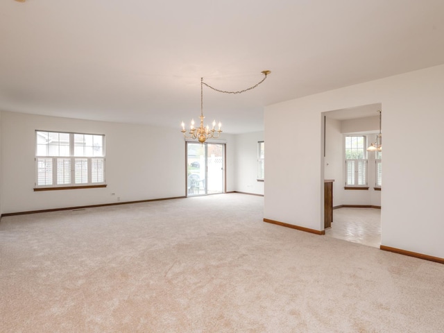 spare room with light colored carpet, baseboards, a notable chandelier, and plenty of natural light