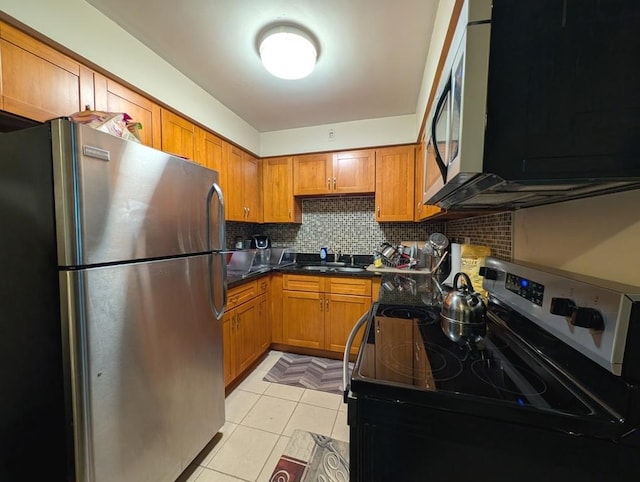 kitchen with appliances with stainless steel finishes, a sink, brown cabinetry, light tile patterned floors, and backsplash