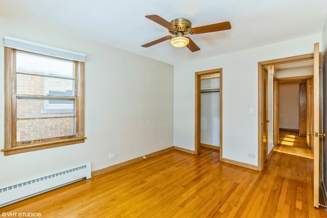 unfurnished bedroom featuring a baseboard heating unit, light wood-type flooring, baseboards, a ceiling fan, and a closet