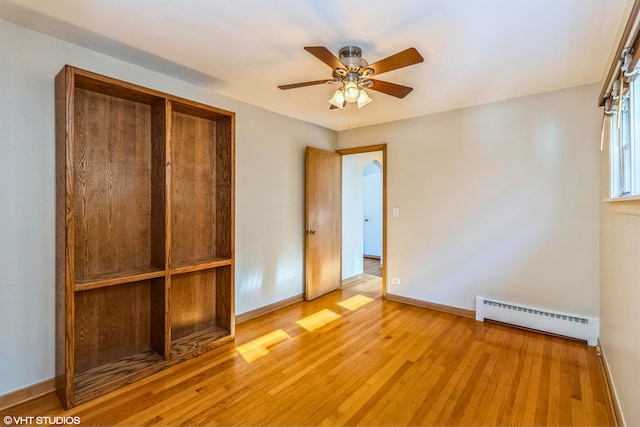 unfurnished bedroom featuring a baseboard heating unit, baseboards, light wood-style floors, a closet, and ceiling fan
