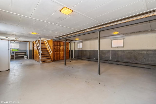 basement with freestanding refrigerator, stairs, and a baseboard radiator