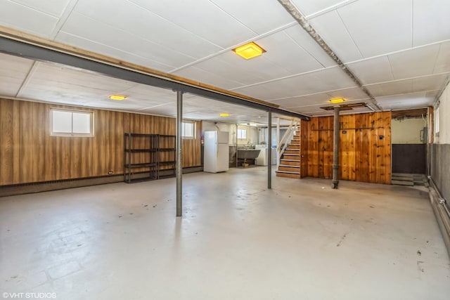 basement featuring a sink, freestanding refrigerator, stairs, washer / clothes dryer, and wooden walls