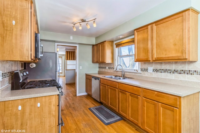 kitchen featuring a sink, light wood-style floors, stainless steel appliances, light countertops, and backsplash