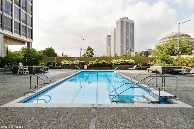 community pool with a patio, fence, and a city view