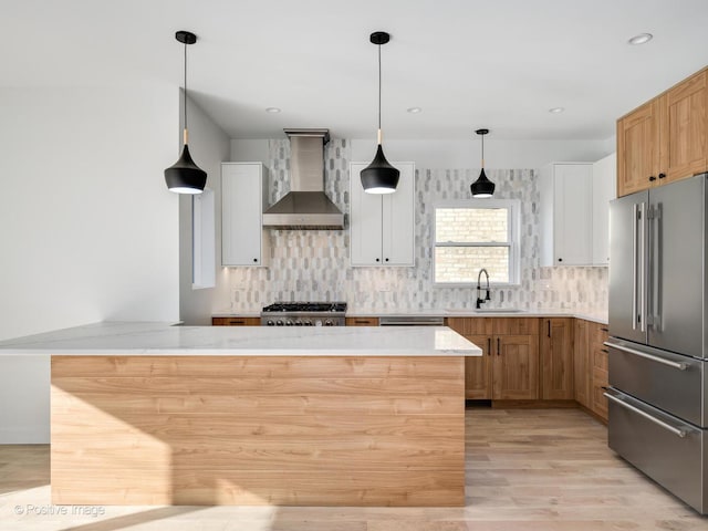 kitchen featuring wall chimney exhaust hood, a sink, high end refrigerator, light wood-type flooring, and range