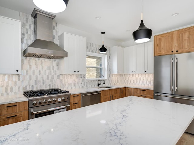kitchen featuring high end appliances, a sink, wall chimney exhaust hood, light stone countertops, and tasteful backsplash