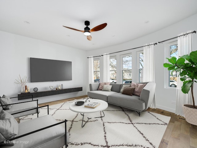 living area featuring wood finished floors, a ceiling fan, and baseboards