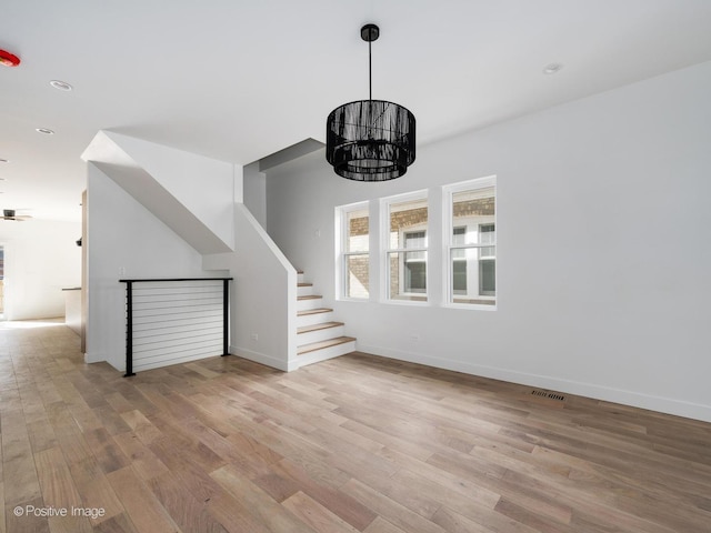 unfurnished living room with wood finished floors, visible vents, baseboards, a chandelier, and stairs