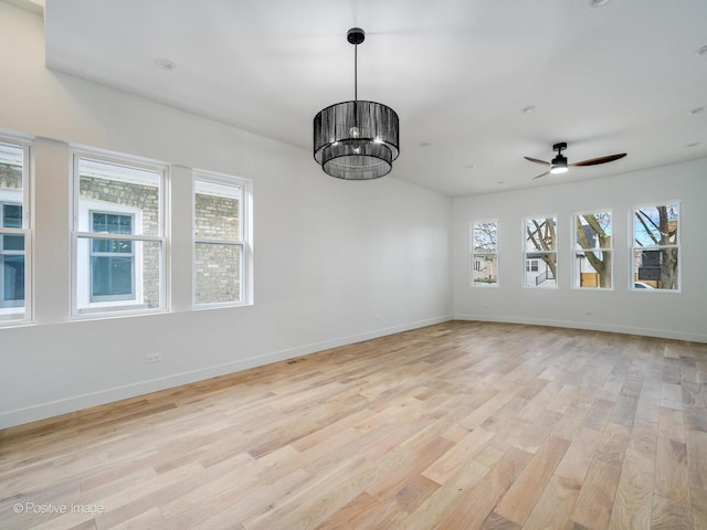 unfurnished dining area with ceiling fan with notable chandelier, light wood-style flooring, baseboards, and a healthy amount of sunlight