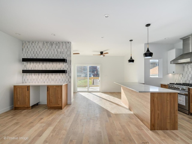 kitchen with light wood-style flooring, high end stove, ceiling fan, light countertops, and a kitchen island
