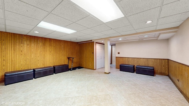 finished basement featuring a paneled ceiling, wood walls, and a wainscoted wall