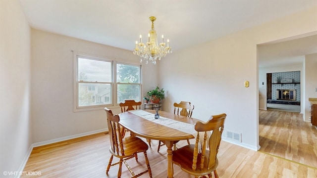 dining room featuring baseboards, visible vents, a brick fireplace, a notable chandelier, and light wood-style floors