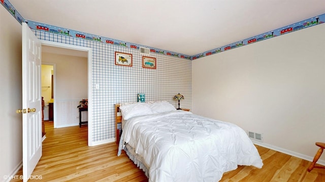 bedroom with baseboards, light wood finished floors, and visible vents