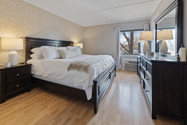 bedroom with an accent wall, a wall unit AC, wallpapered walls, and light wood-type flooring