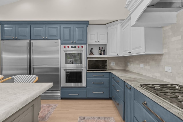 20 Colony Ln, Deerfield, IL 60015 - kitchen featuring stainless steel appliances, blue cabinets, wall chimney range hood, white cabinets, and tasteful backsplash