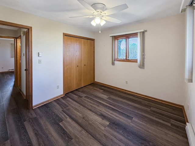 unfurnished bedroom featuring baseboard heating, baseboards, dark wood-type flooring, and a closet