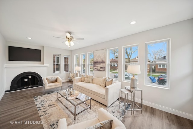 living room featuring ceiling fan, a brick fireplace, wood finished floors, baseboards, and recessed lighting