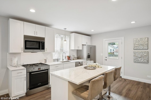 kitchen featuring a kitchen island, a kitchen bar, appliances with stainless steel finishes, a sink, and dark wood-type flooring