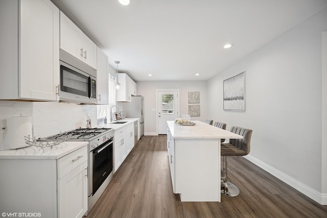 kitchen featuring baseboards, a breakfast bar area, stainless steel microwave, dark wood finished floors, and gas stove