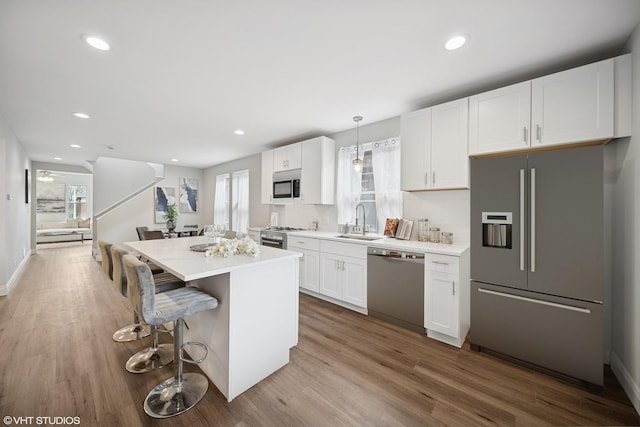 kitchen with a kitchen island, light countertops, white cabinetry, a sink, and appliances with stainless steel finishes