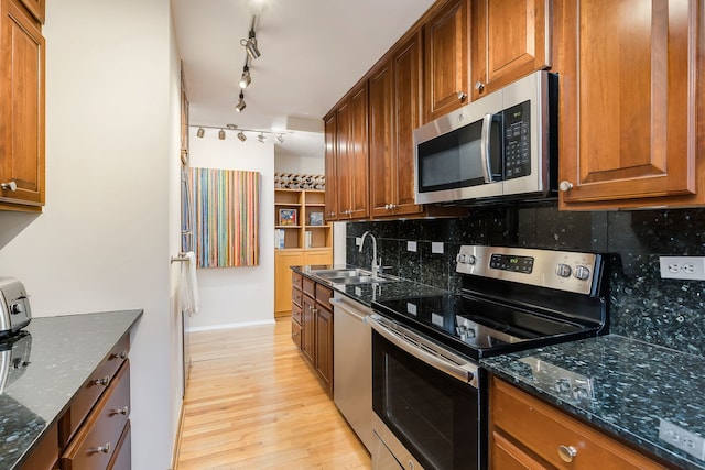 kitchen with appliances with stainless steel finishes, a sink, decorative backsplash, light wood-style flooring, and brown cabinetry