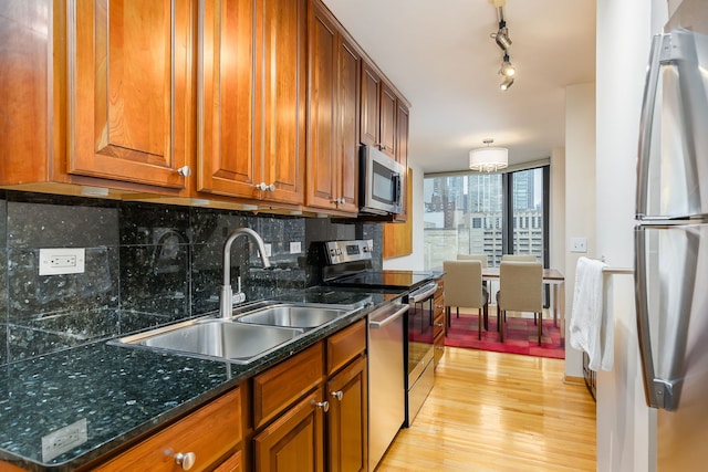 kitchen featuring appliances with stainless steel finishes, a sink, brown cabinets, light wood-style floors, and decorative backsplash