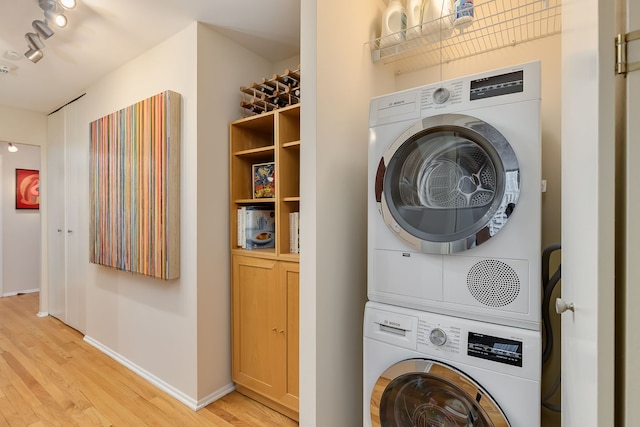 laundry room featuring stacked washing machine and dryer, light wood-style floors, rail lighting, and baseboards