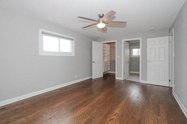 unfurnished bedroom with baseboards, a spacious closet, dark wood finished floors, and multiple windows
