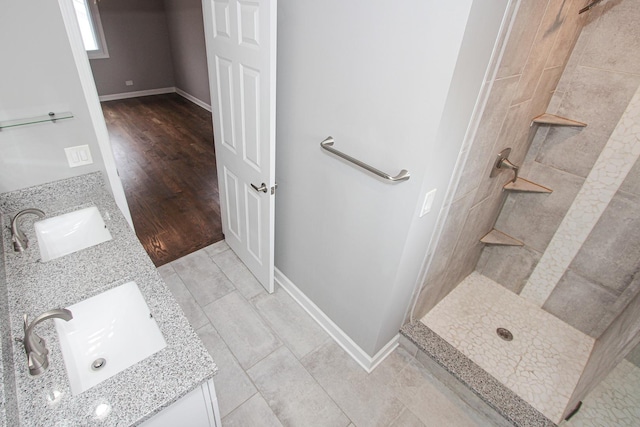 bathroom with baseboards, a sink, double vanity, and tiled shower