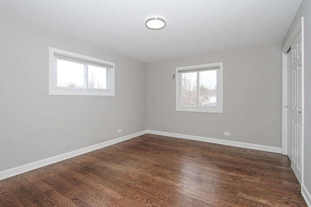 unfurnished bedroom featuring baseboards, dark wood-style floors, a closet, and multiple windows