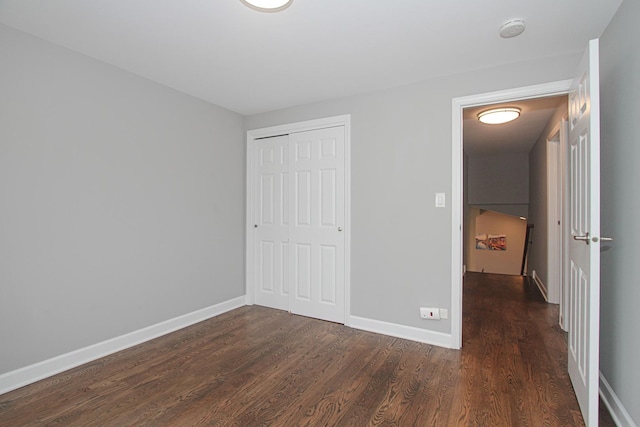 unfurnished bedroom featuring dark wood finished floors, baseboards, and a closet