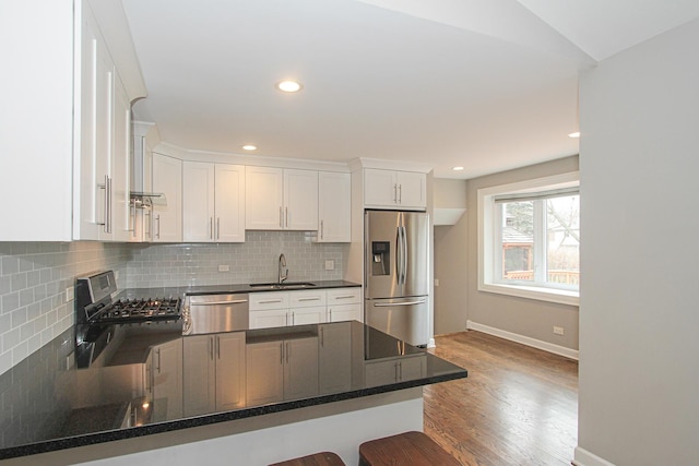 kitchen with wood finished floors, a sink, white cabinetry, backsplash, and appliances with stainless steel finishes