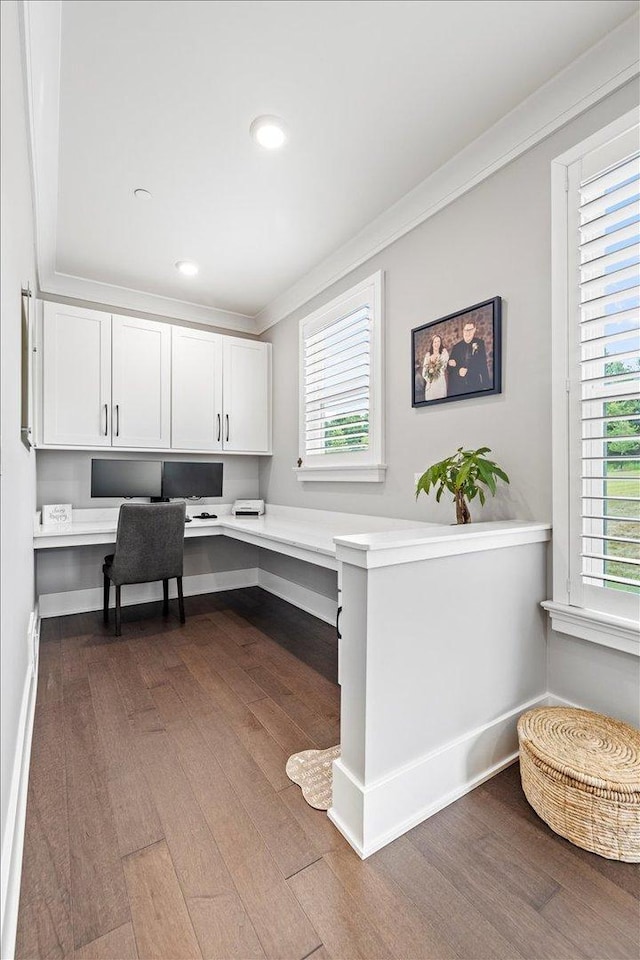office space featuring crown molding, plenty of natural light, built in desk, and dark wood finished floors