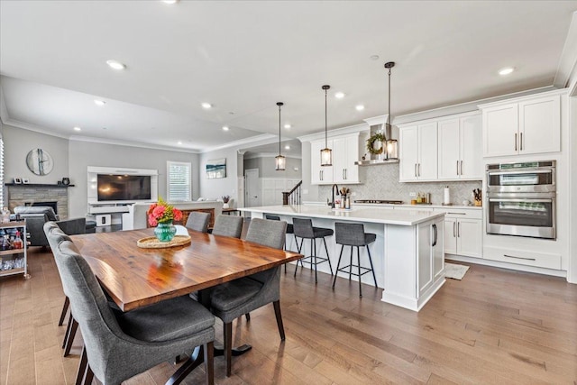 dining area featuring recessed lighting, a fireplace, light wood-style floors, and ornamental molding