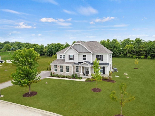 view of front of home with stone siding, a shingled roof, a front lawn, and board and batten siding