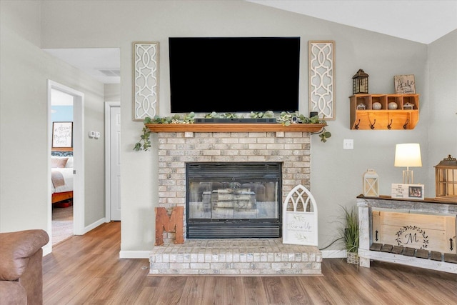 living area with vaulted ceiling, wood finished floors, a brick fireplace, and baseboards