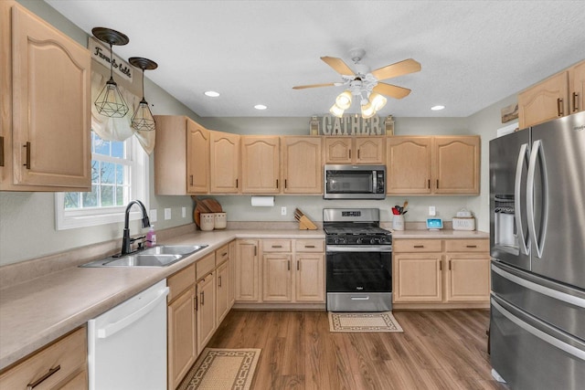 kitchen featuring stainless steel appliances, light countertops, a sink, ceiling fan, and light brown cabinets