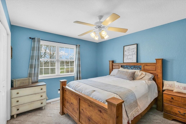 bedroom with ceiling fan, light carpet, a textured wall, and a textured ceiling