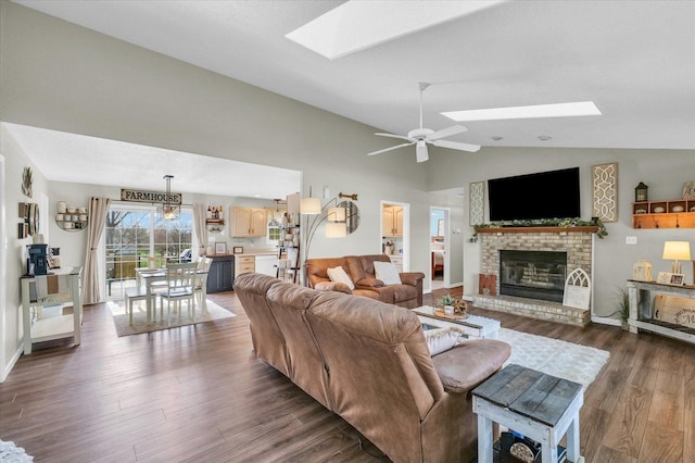 living room with a fireplace, dark wood finished floors, lofted ceiling with skylight, and ceiling fan