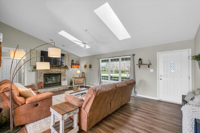 living area featuring wood finished floors, a ceiling fan, lofted ceiling with skylight, baseboards, and a brick fireplace