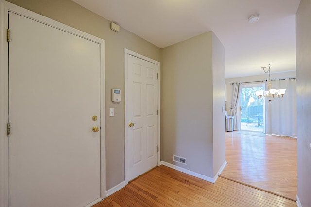 foyer entrance featuring visible vents, an inviting chandelier, baseboards, and light wood-type flooring