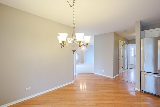 unfurnished dining area featuring light wood finished floors, an inviting chandelier, and baseboards