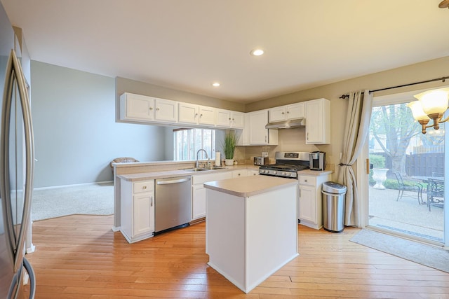 kitchen with stainless steel appliances, under cabinet range hood, light countertops, a sink, and white cabinetry