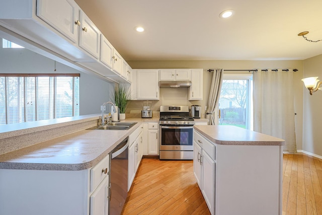 kitchen featuring stainless steel appliances, light wood-style floors, under cabinet range hood, light countertops, and a sink