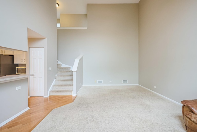 unfurnished living room featuring baseboards, stairway, visible vents, and light carpet