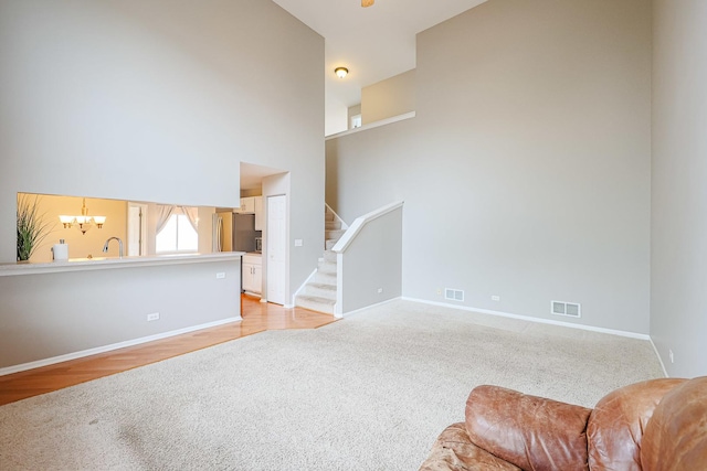 unfurnished living room with an inviting chandelier, visible vents, light carpet, and baseboards